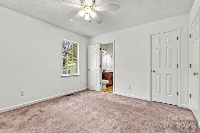 unfurnished bedroom featuring connected bathroom, a textured ceiling, light carpet, and ceiling fan