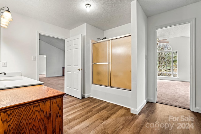 bathroom featuring bath / shower combo with glass door, wood-type flooring, lofted ceiling, and a textured ceiling