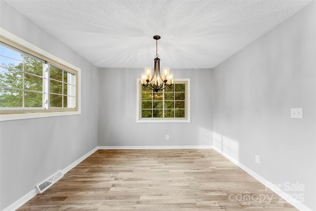 unfurnished room with a textured ceiling, an inviting chandelier, and light hardwood / wood-style flooring