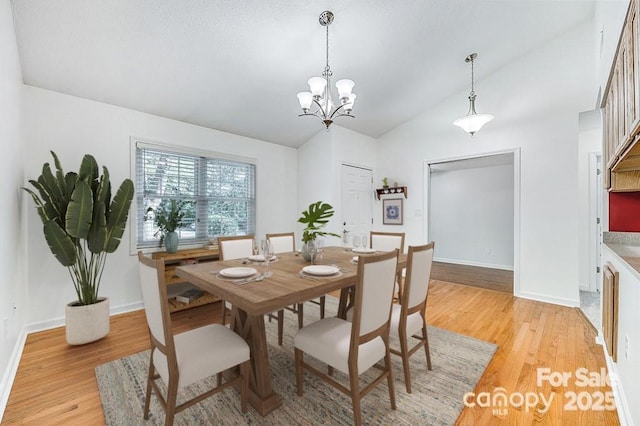 dining area featuring a chandelier, vaulted ceiling, and light hardwood / wood-style flooring