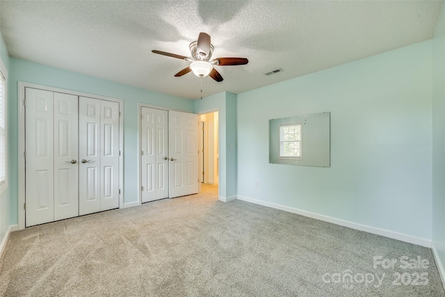 unfurnished bedroom with light carpet, a textured ceiling, two closets, and ceiling fan