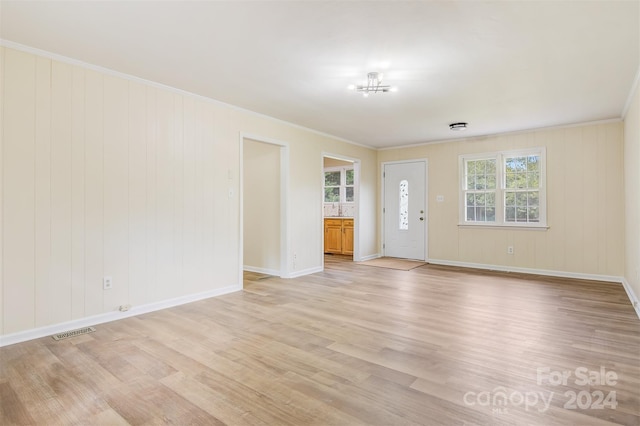 unfurnished living room featuring ornamental molding, wooden walls, and light hardwood / wood-style floors