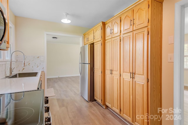 kitchen featuring light wood-type flooring, stainless steel refrigerator, decorative backsplash, and sink