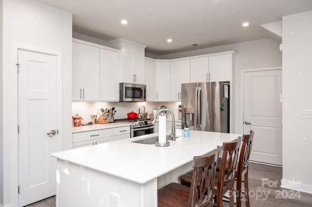 kitchen with wood-type flooring, sink, white cabinets, stainless steel appliances, and a center island with sink