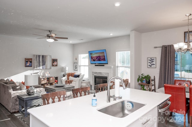 kitchen with dark wood-type flooring, sink, ceiling fan with notable chandelier, a fireplace, and a center island with sink