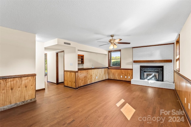 unfurnished living room featuring wood walls, ceiling fan, a fireplace, hardwood / wood-style flooring, and a textured ceiling