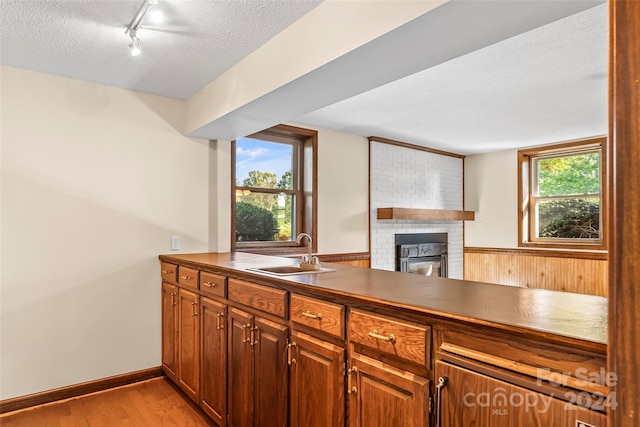 kitchen featuring light wood-type flooring, sink, kitchen peninsula, track lighting, and a textured ceiling