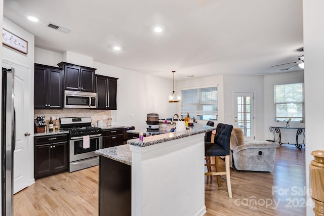 kitchen with a kitchen island with sink, light stone countertops, pendant lighting, light hardwood / wood-style floors, and stainless steel appliances