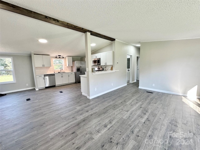 unfurnished living room with a textured ceiling, lofted ceiling with beams, sink, and light hardwood / wood-style flooring