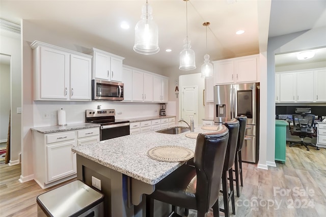 kitchen with appliances with stainless steel finishes, white cabinets, hanging light fixtures, and light wood-type flooring