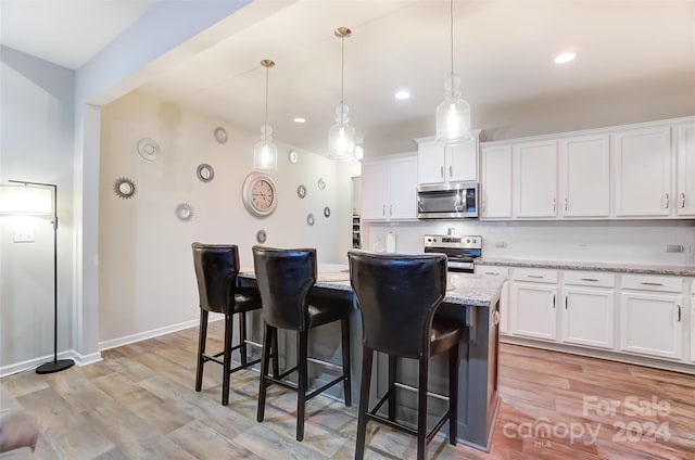 kitchen featuring a kitchen island, decorative light fixtures, light wood-type flooring, white cabinetry, and appliances with stainless steel finishes