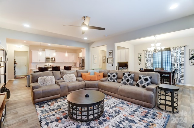 living room with light wood-type flooring and ceiling fan with notable chandelier