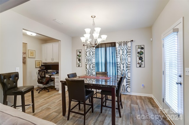 dining area featuring built in desk, a chandelier, and light hardwood / wood-style floors