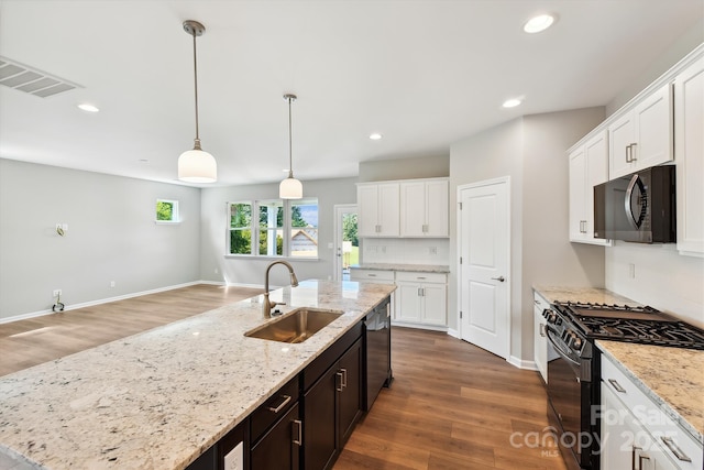 kitchen featuring white cabinets, black appliances, decorative light fixtures, sink, and a center island with sink