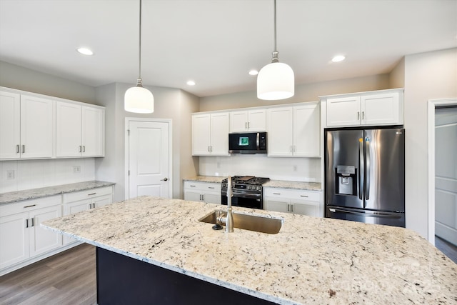 kitchen featuring decorative light fixtures, white cabinets, stainless steel appliances, and a center island with sink