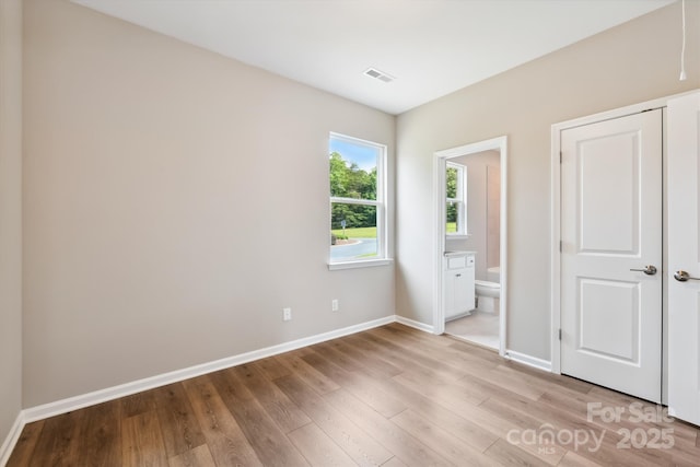 unfurnished bedroom with light hardwood / wood-style floors and connected bathroom