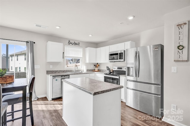 kitchen with a wealth of natural light, a center island, white cabinets, appliances with stainless steel finishes, and wood-type flooring