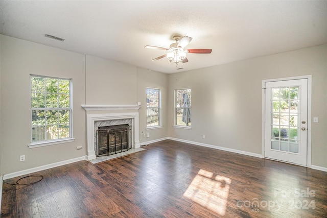 unfurnished living room with a high end fireplace, a healthy amount of sunlight, ceiling fan, and dark hardwood / wood-style flooring