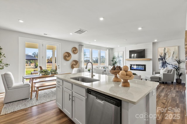 kitchen featuring a large fireplace, a kitchen island with sink, sink, dishwasher, and white cabinetry