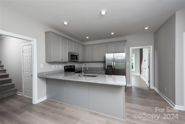 kitchen with kitchen peninsula, light stone countertops, light wood-type flooring, sink, and stainless steel appliances