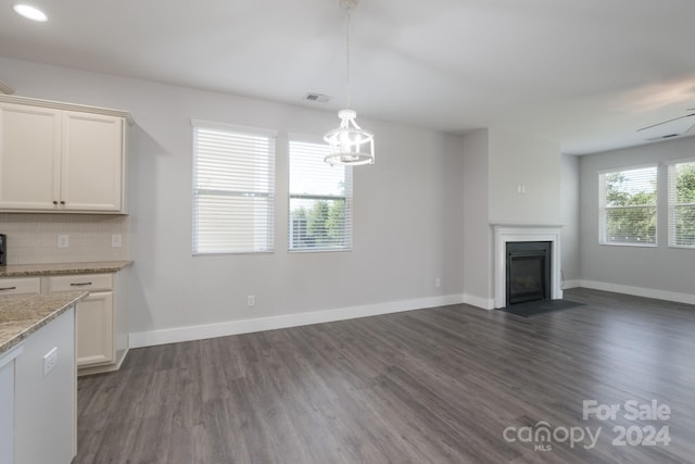 unfurnished living room featuring ceiling fan with notable chandelier and dark hardwood / wood-style flooring