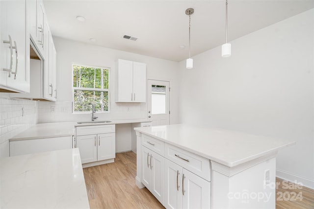 kitchen with light hardwood / wood-style flooring, white cabinets, decorative light fixtures, and sink