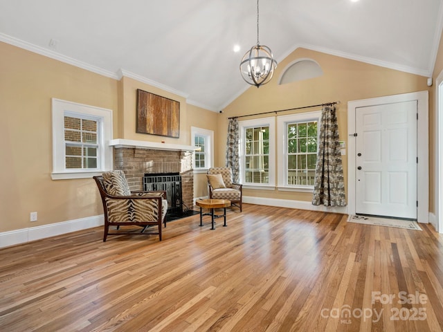 sitting room with lofted ceiling, light hardwood / wood-style floors, crown molding, a brick fireplace, and an inviting chandelier