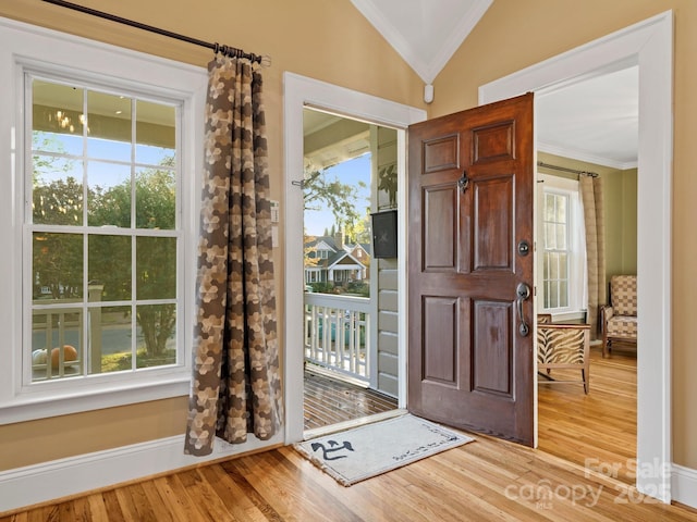 foyer entrance featuring ornamental molding, lofted ceiling, plenty of natural light, and light hardwood / wood-style flooring