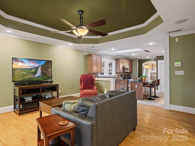 living room with crown molding, a raised ceiling, ceiling fan, and light wood-type flooring