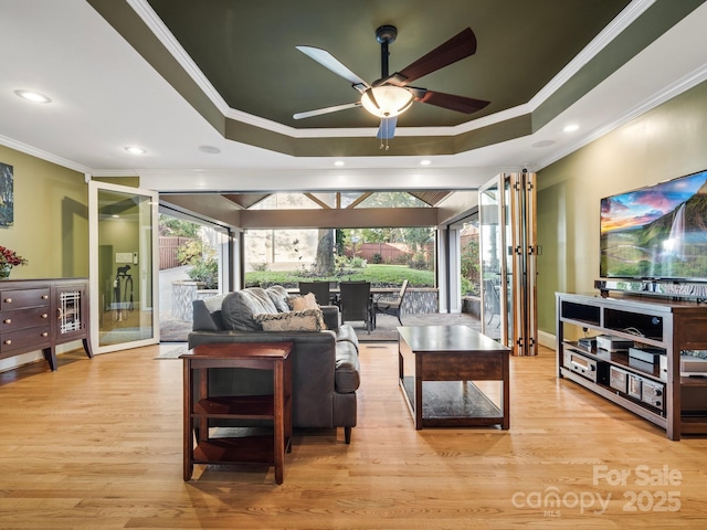 living room featuring crown molding, plenty of natural light, a raised ceiling, and light hardwood / wood-style flooring