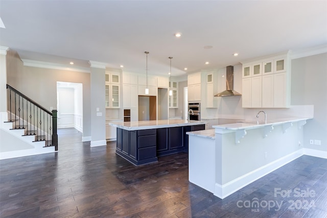 kitchen featuring white cabinets, hanging light fixtures, a kitchen island, wall chimney exhaust hood, and dark wood-type flooring