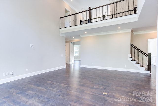 unfurnished living room with a towering ceiling, ornamental molding, and dark hardwood / wood-style flooring