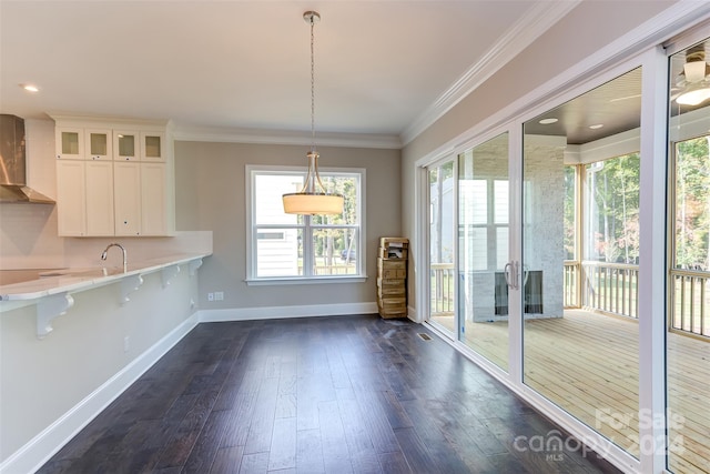 kitchen with white cabinets, wall chimney exhaust hood, decorative light fixtures, dark hardwood / wood-style floors, and crown molding