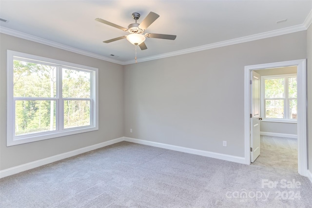 empty room featuring crown molding, ceiling fan, light colored carpet, baseboards, and visible vents