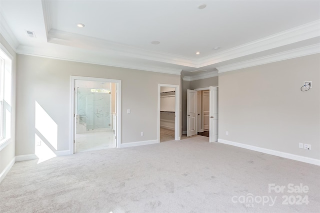 unfurnished bedroom featuring a walk in closet, light colored carpet, connected bathroom, and a raised ceiling