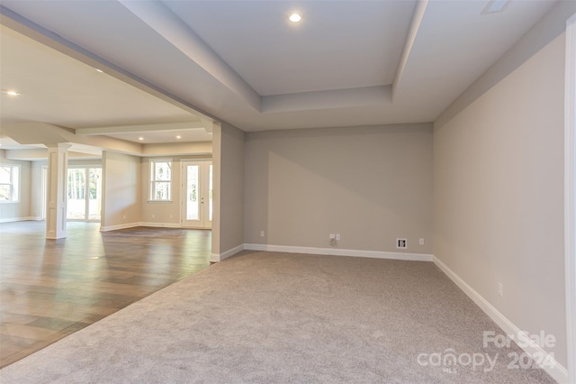 empty room with wood-type flooring, a raised ceiling, and decorative columns