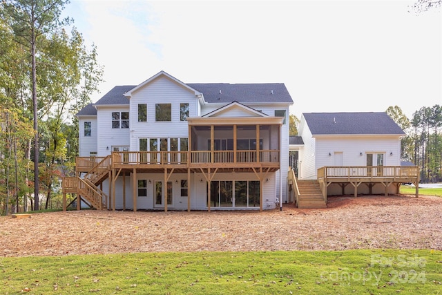 back of property featuring a deck, a sunroom, and a lawn