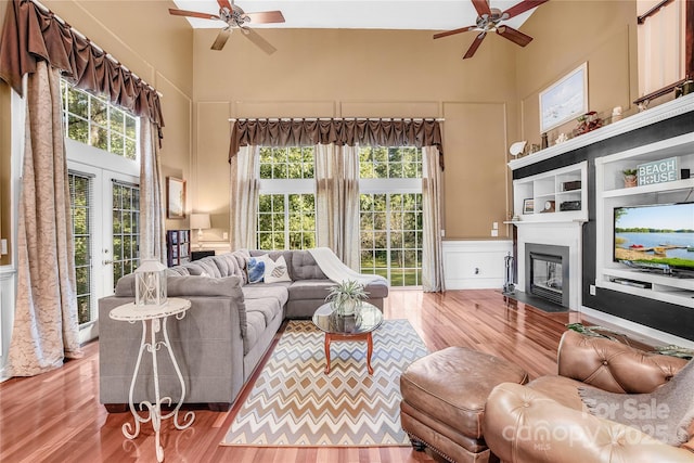 living room with french doors, a towering ceiling, wood-type flooring, and ceiling fan