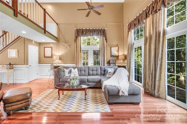 living room featuring ceiling fan, a towering ceiling, light wood-type flooring, and french doors