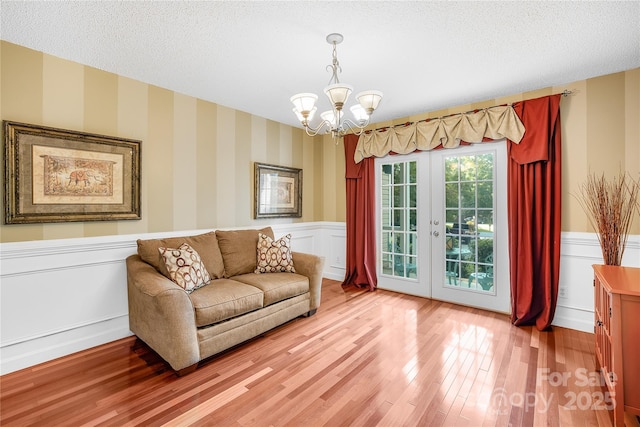 living area featuring french doors, a chandelier, hardwood / wood-style floors, and a textured ceiling