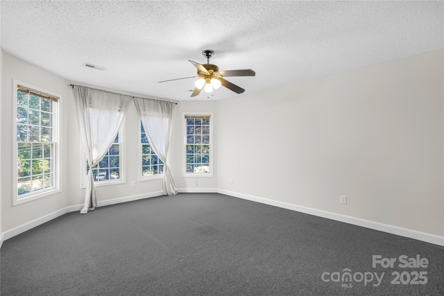 spare room with a textured ceiling, ceiling fan, and dark colored carpet