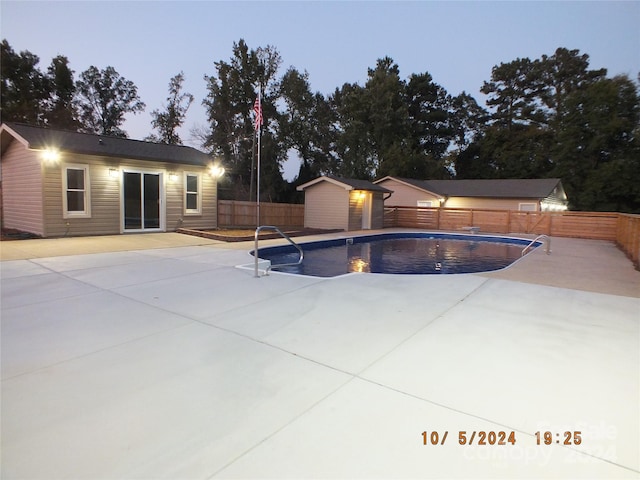 pool at dusk featuring a storage unit and a patio area