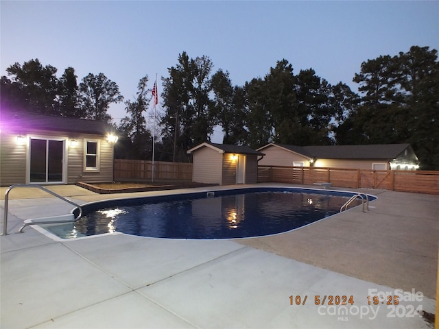 pool at dusk featuring a patio and an outdoor structure