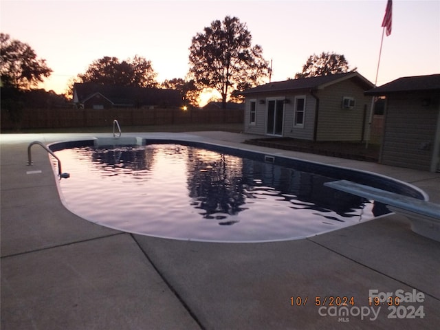 pool at dusk with a diving board, an outdoor structure, and a patio area