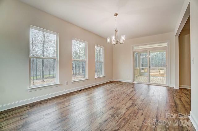 unfurnished dining area with a notable chandelier, plenty of natural light, and hardwood / wood-style flooring