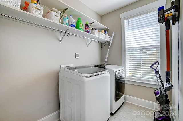 clothes washing area with light tile patterned floors, washer and dryer, and a wealth of natural light