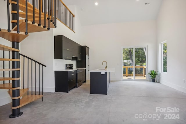 kitchen with black electric range, a kitchen bar, a kitchen island with sink, and a towering ceiling