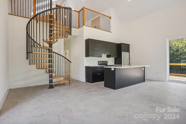 interior space with an island with sink, sink, stainless steel range with electric cooktop, and high vaulted ceiling