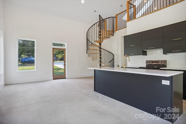 kitchen with a high ceiling, stainless steel electric range, sink, and a kitchen island with sink