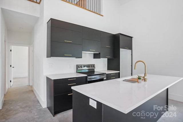 kitchen featuring stainless steel electric range oven, sink, an island with sink, and a towering ceiling